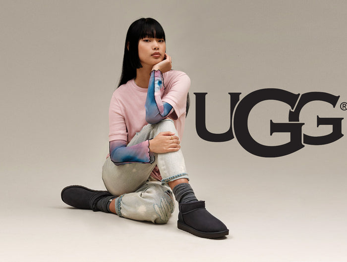 Person sitting on ground wearing black Ugg boots sold by Boot World