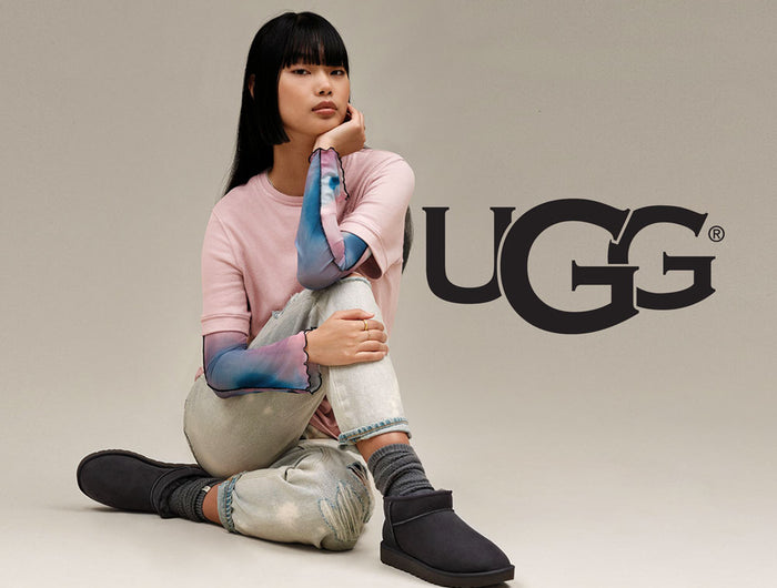 Person sitting on ground wearing black Ugg boots sold by Boot World